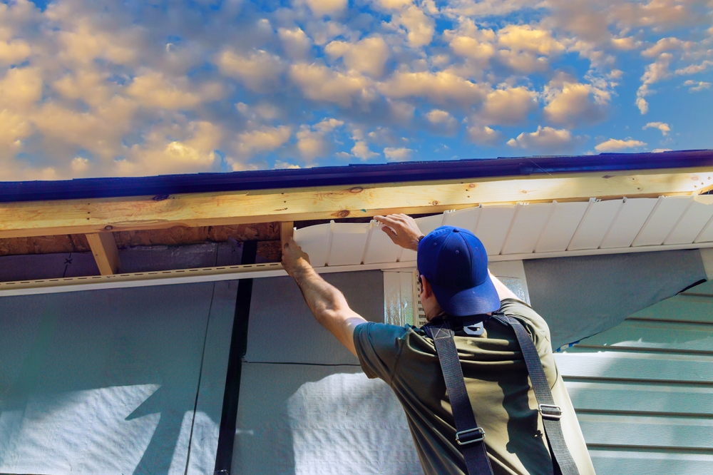 Professional roofing contractor installing white vinyl soffit panels beneath a residential roof eave during exterior home renovation.